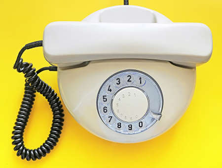 Biege old telephone with rotary dial on yellow background. Flat lay. Top viewの写真素材