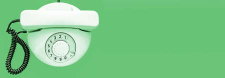 White old telephone with rotary dial on green background. Flat lay. Top view. Banner. Place for textの写真素材