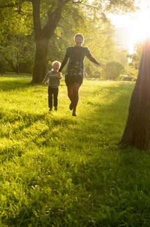 Mother and young son happily run on the lawn in the sun.の写真素材
