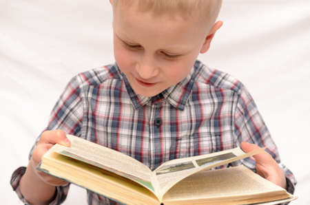 A five-year-old boy is reading a book on the bed.の写真素材