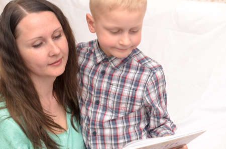 A five-year-old boy is reading a book on the bed.の写真素材
