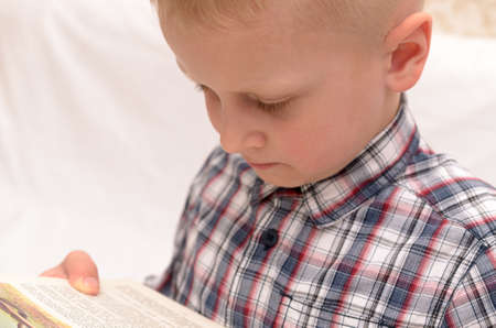 A five-year-old boy is reading a book on the bed.の写真素材