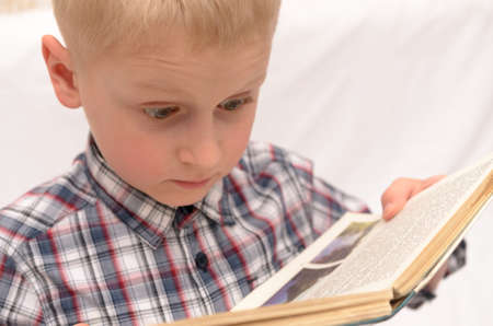 A five-year-old boy is reading a book on the bed.の写真素材
