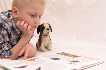 A five-year-old boy is reading a book on the bed.の写真素材