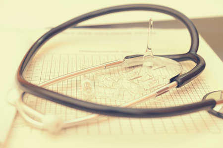 A phonendoscope lies on the doctors desk along with a pen, a history of the disease and ampoules with a medicine.の写真素材