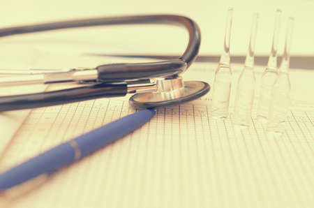 A phonendoscope lies on the doctor's desk along with a pen, a history of the disease and ampoules with a medicineの写真素材