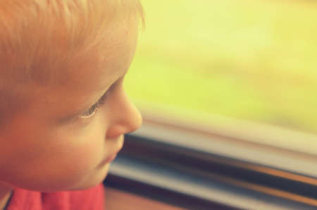 The boy looks out the window of the train car