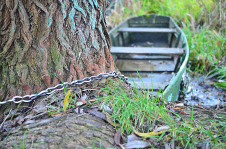The old boat is tied to a tree trunk by a chainの写真素材