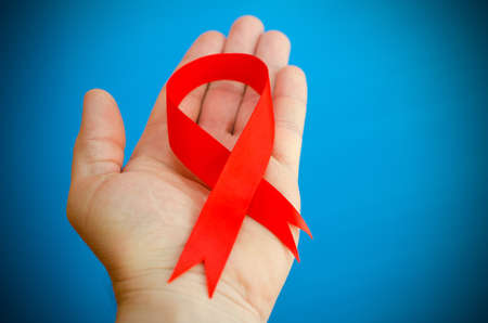 Red folded ribbon in hand on a blue background as a symbol of hemophilia