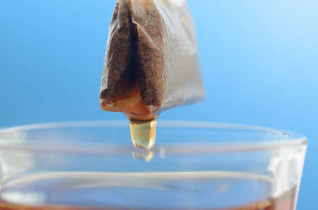 A tea bag over a glass mug with hot water close-up on a blue backgroundの写真素材