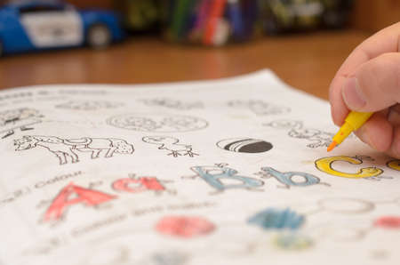 A child's hand writes and displays English letters in a notebook and alphabet with a pencil and felt-tip penの写真素材