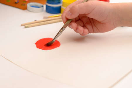 A childs hand draws gouache on white paper with a brush.の写真素材