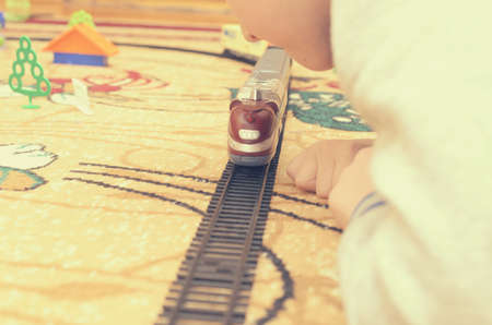 A blond boy plays with a toy train in a room on the carpet