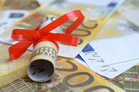 Rolls of money in a gift ribbon on bills of dollars and euros