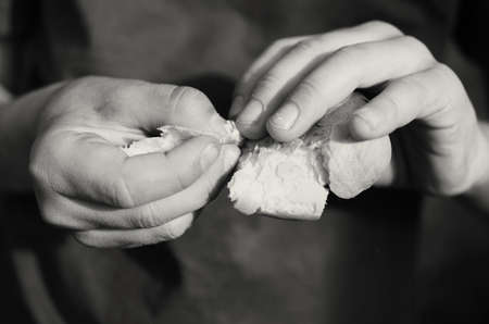 The hands of a beggar hungry boy hold and break a piece of breadの写真素材