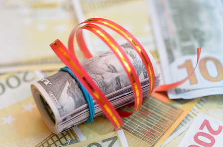 Rolls of money in a gift ribbon on bills of dollars and euros.の写真素材