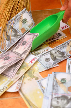 Broom sweep a lot of dollar and euro bills in the scoop.の写真素材