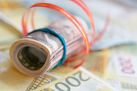 Rolls of money in a gift ribbon on bills of dollars and euros
