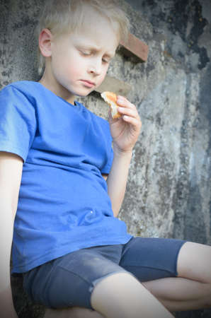 A hungry dirty boy greedily eats a crust of bread against the wallの写真素材