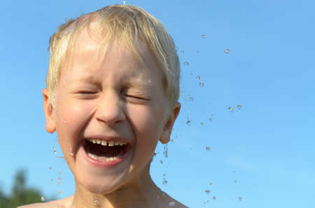 On the head of a light-haired boy pours a stream of water against the blue sky and he rejoicesの写真素材
