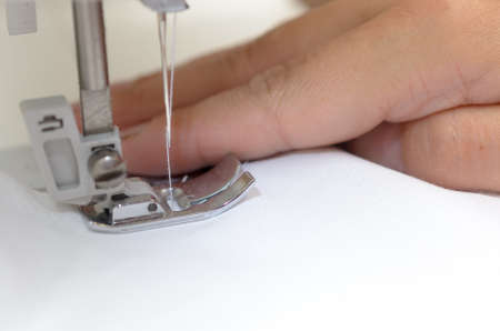 Hands seamstresses with white material behind the sewing machine