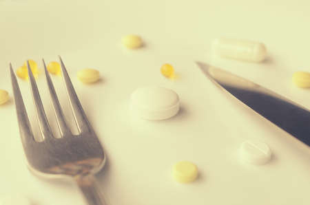 Pills in a white plate with fork and knife. The concept of imposing drugsの写真素材