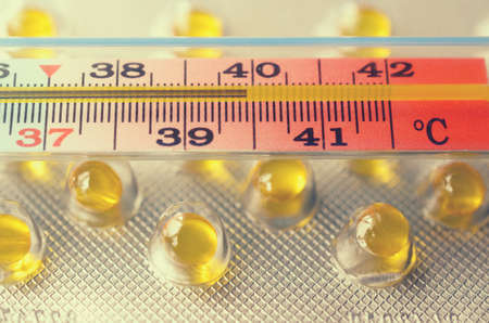 Medical mercury thermometer on the background of the plates with pills