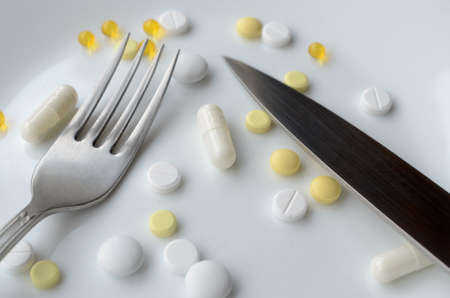 Pills in a white plate with fork and knife. The concept of imposing drugsの写真素材