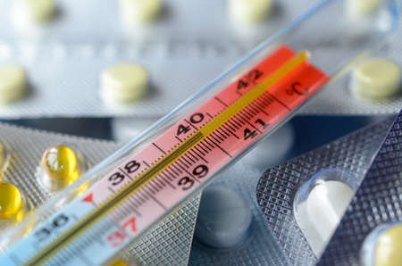 Medical mercury thermometer on the background of the plates with pills