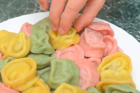 Multicolored ravioli for a festive menu are cooked in a pan and on a plateの写真素材