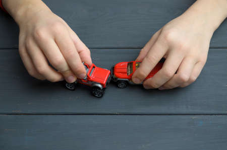 The hand of the child plays with a red typewriter on a wooden surface of a dark color