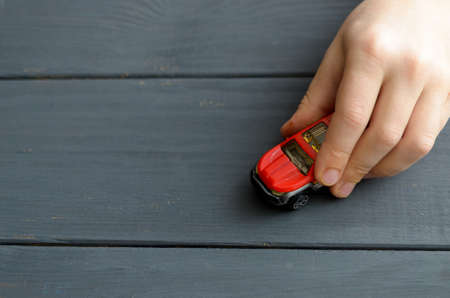 The hand of the child plays with a red typewriter on a wooden surface of a dark colorの写真素材
