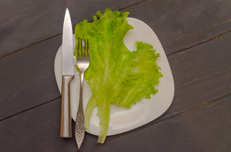 Salad leaves on a white plate with fork and knife. Gray wooden background. The concept of healthy eatingの写真素材