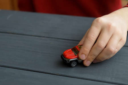 The hand of the child plays with a red typewriter on a wooden surface of a dark color
