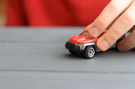 The hand of the child plays with a red typewriter on a wooden surface of a dark color