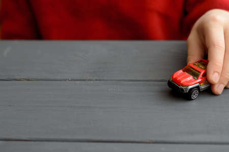 The hand of the child plays with a red typewriter on a wooden surface of a dark colorの写真素材