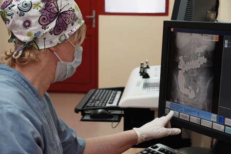 A woman radiologist behind the monitor makes an X-ray correction.