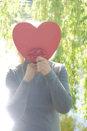 The girl sends an air kiss with large red decorative lips with a paper heart. World Kiss Day.の写真素材