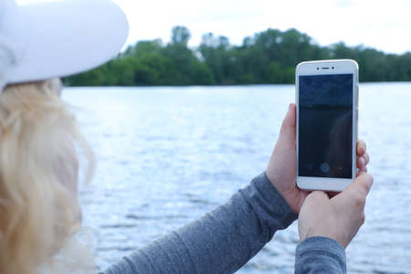 A girl in a white cap photographs the water landscape on the phone. St. Veronicas Day Photographers Day .の写真素材