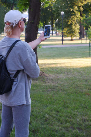 A tourist girl in a white cap is taking a photo on the phone.