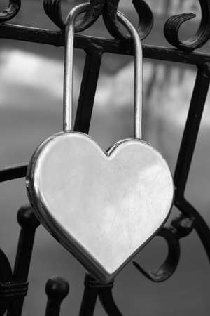 Metal silver door lock in the shape of a heart on the fence as a symbol of eternal love.の写真素材