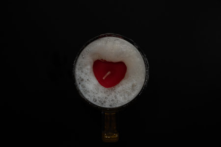 Red heart on beer foam in a glass. Dark background.の写真素材
