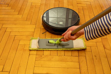 Robot vacuum cleaner on lacquered parquet against a conventional mop.の写真素材