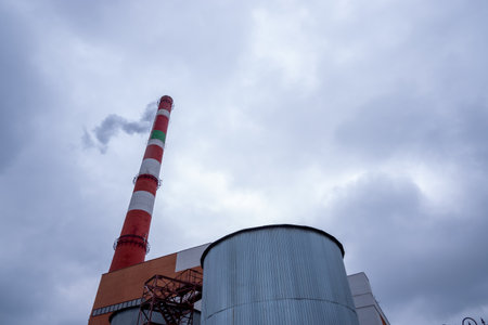 The red-and-white factory chimney exudes smoke against the background of a gloomy sky. The concept of environmental safetyの写真素材