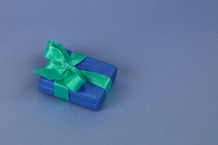 A blue gift box with a green ribbon on a blue paper background.の写真素材