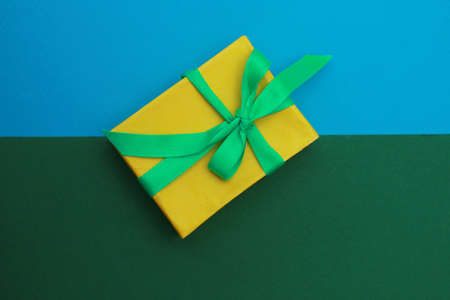 Yellow paper box with green ribbon on double background of blue and green. . Holiday concept. Christmas gift.の写真素材