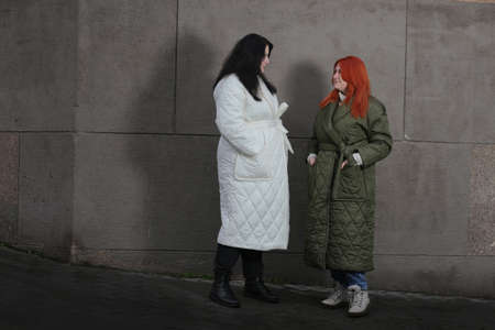 A woman in a white coat with black hair and a brown-haired girl in a green raincoat stand against an...