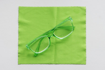 Folded glasses with a green transparent frame lie on a green cleaning cloth.の写真素材
