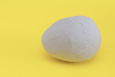 Handmade egg covered with gray plaster on a yellow background. Minimal Easter.の写真素材