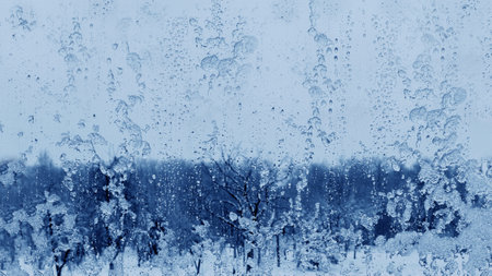 Frozen rain drops on a window with a blurry snowy view. Drops of ice and rain on a window overlooking a winter blue snowy forest.の写真素材